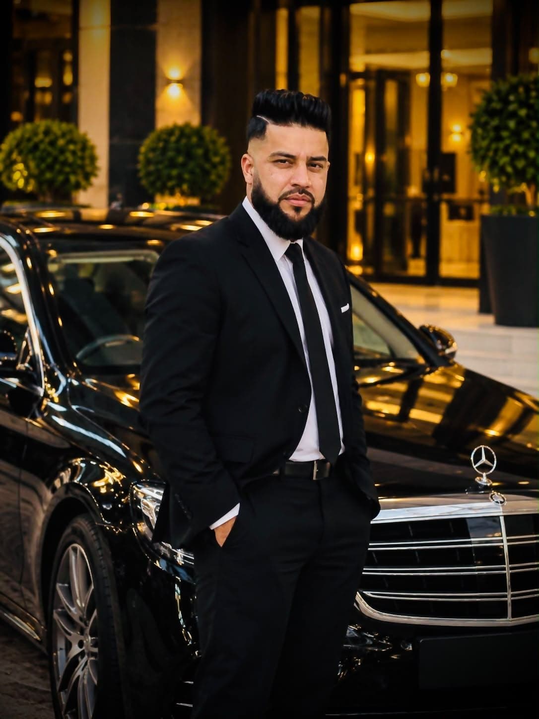 Shahzad Shary, owner of Bespoke Executive Chauffeurs, beside a black Mercedes outside a hotel entrance